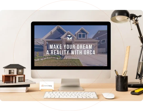 A computer screen on a tidy desk displays a home exterior with the text Make your dream a reality with Orca. The desk also has a model house, business cards, a lamp, and stationery.